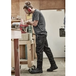 Men's rugged cooling stretch pants in black, featuring cargo pockets, are worn by a person working in a workshop.