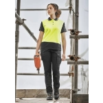 A woman is walking on scaffolding, wearing a yellow and black polo shirt and black cargo pants with a tool in hand.