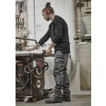 A man wearing black work pants stands by a workshop table, handling tools in a well-equipped space.
