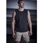 A man wearing a black sleeveless top and beige sports shorts stands in a dimly lit setting. The shorts feature a logo.