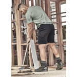 A man in a grey t-shirt and black shorts works on a construction site, holding a broom and wearing sturdy boots.