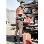 A man wearing orange and navy workwear shorts stands beside a vehicle, holding a drill and a red toolbox.