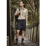 A woman stands on a wooden bridge wearing khaki and navy rugged cooling vented shorts, paired with a button-up shirt and boots.