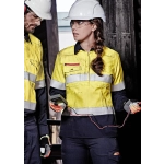 A yellow and navy safety shirt with hooped reflective tape, featuring a logo, worn by a woman in a construction setting.